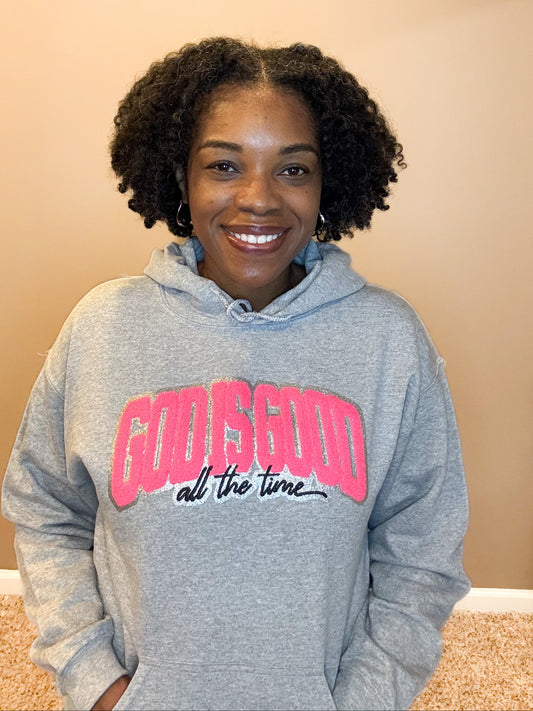 model wearing gray hooded sweatshirt that reads God is Good All the time in chenille pink and black wording