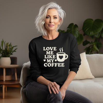 Woman wearing a black sweatshirt with 'Love me like my coffee' text and graphic, sitting on a couch.
