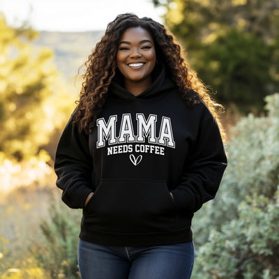 Woman wearing a black hoodie with 'MAMA NEEDS COFFEE' text outdoors.